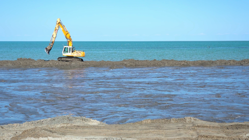 Un escavatore lavora sulla sabbia in spiaggia