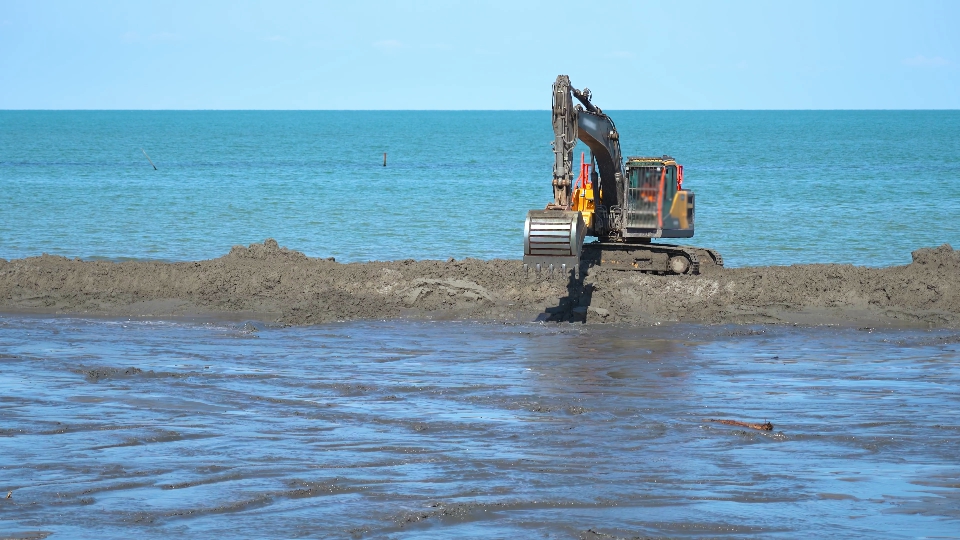 Un escavatore si muove sulla duna di sabbia davanti al mare blu