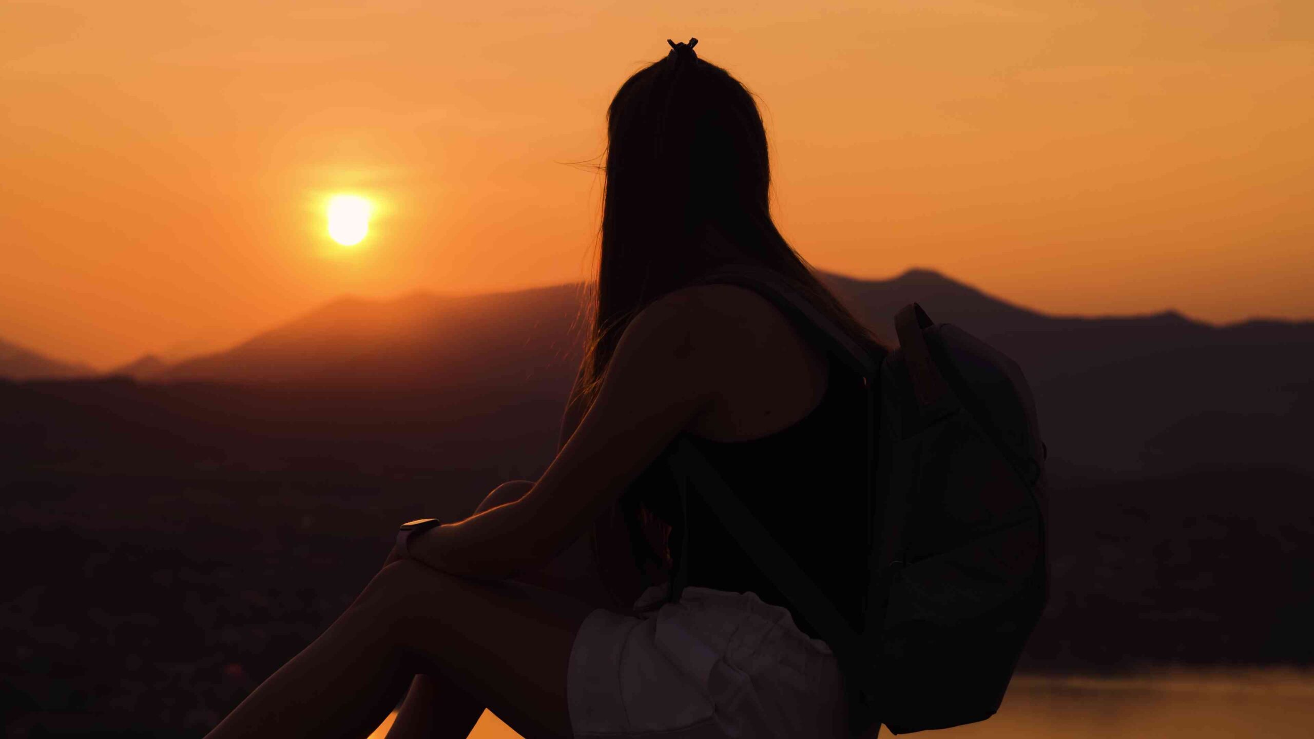 Girl looks silhouette of mountains at sunset