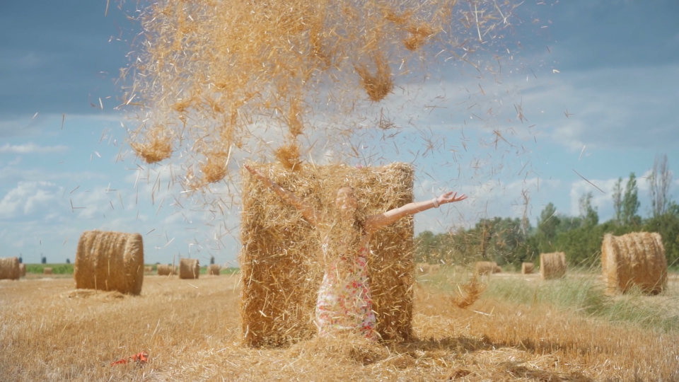 Happy girl throws up straw on the field in the sun