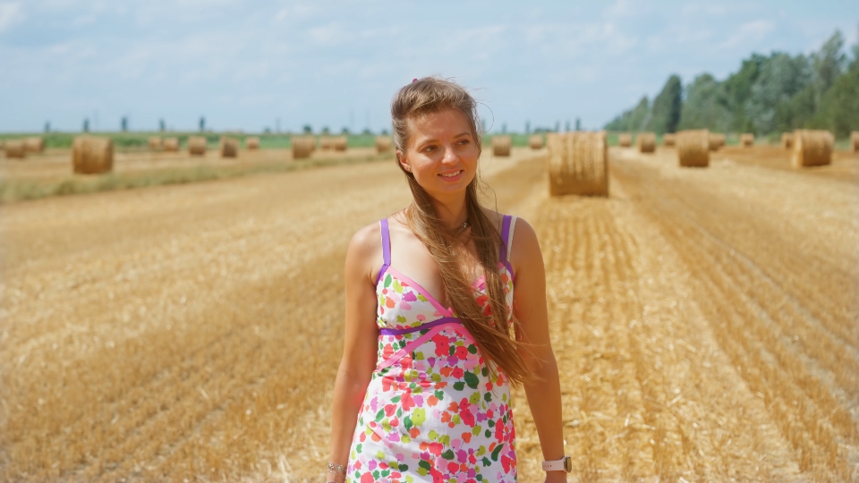 Donna sorridente cammina sul campo con paglia in estate