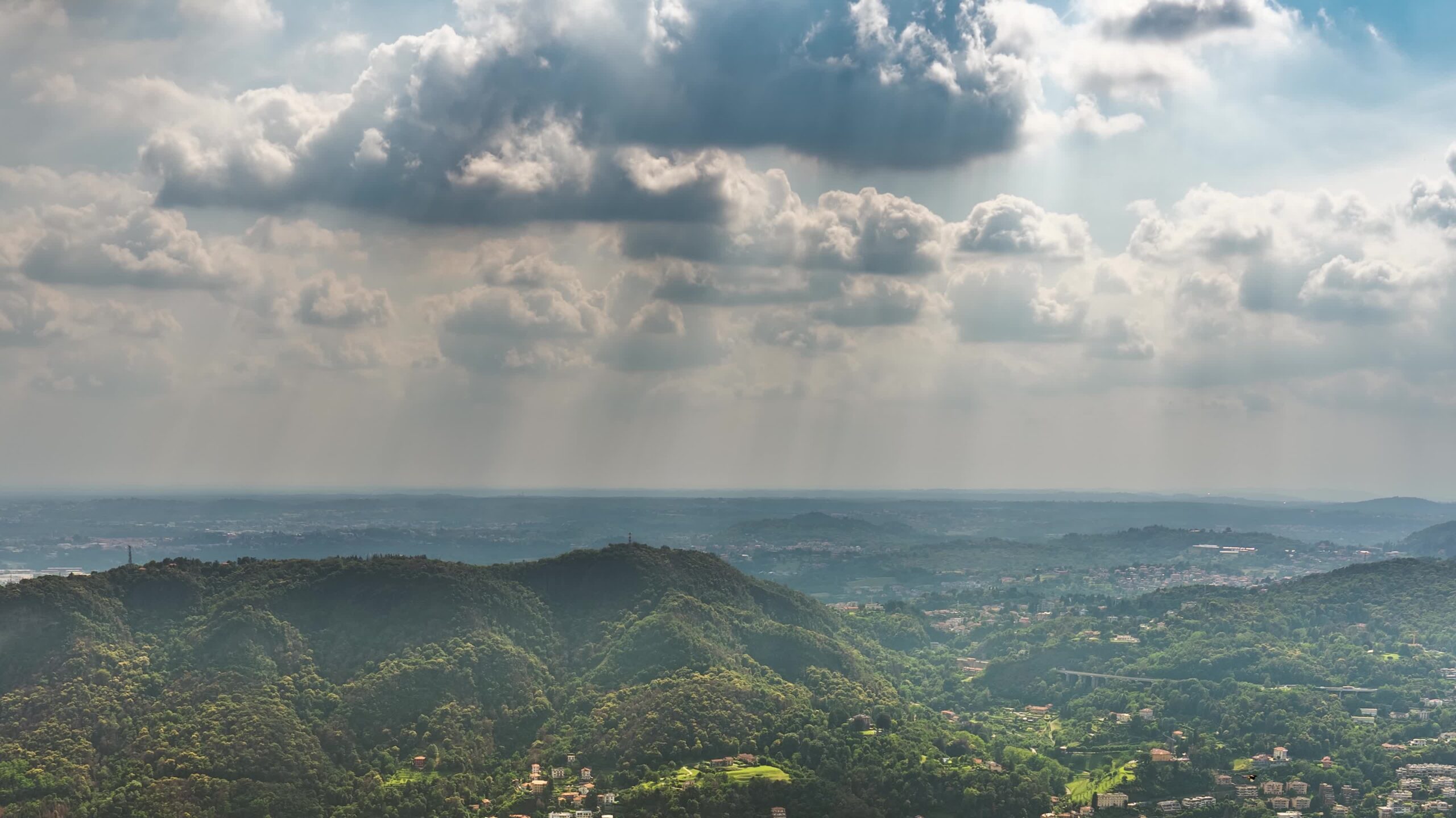 Sky with sunbeams above hills covered with green forest