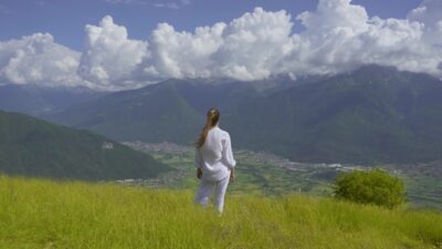 Woman in white with open arms in front of nature landscape in the mountains