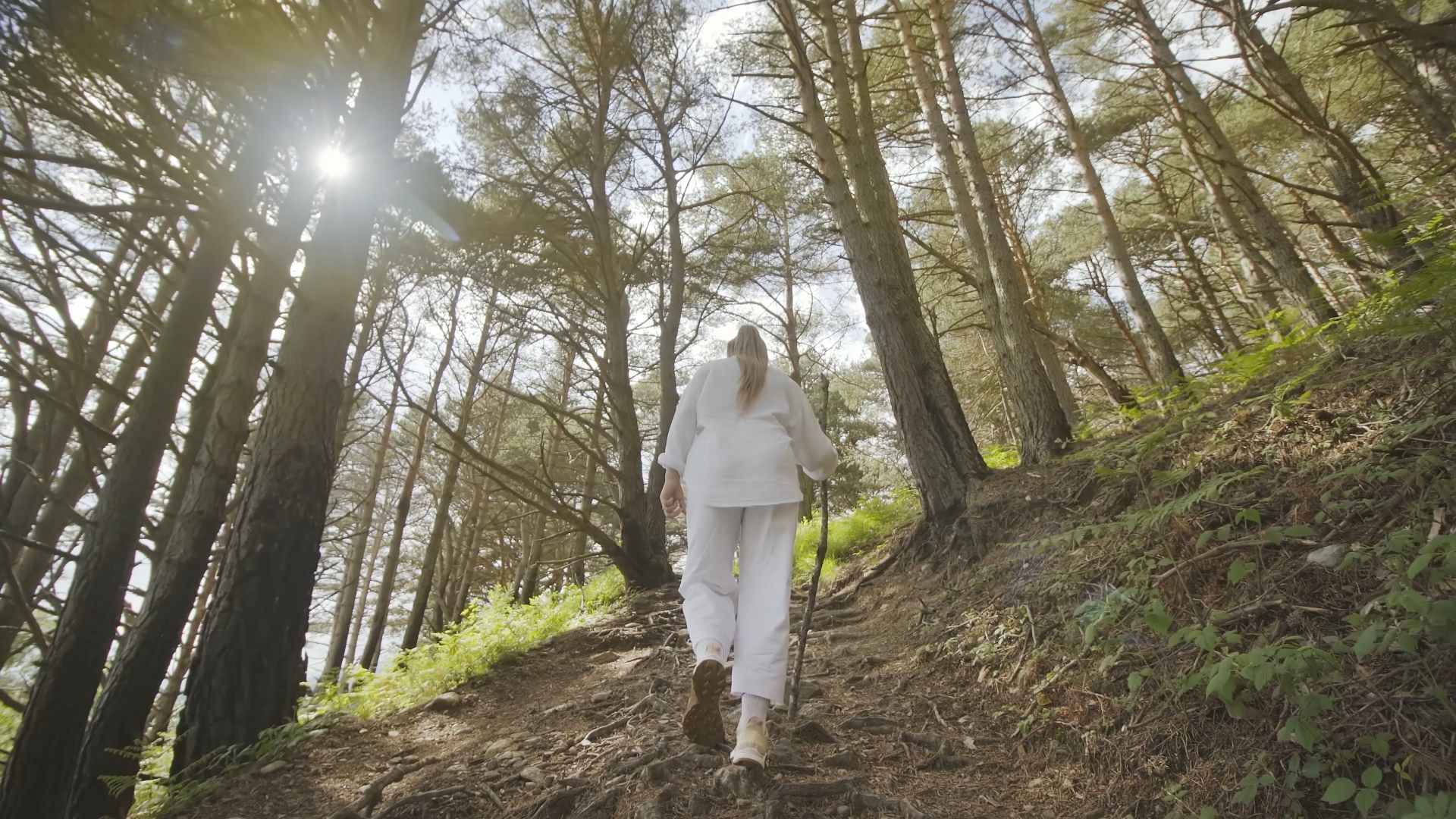 Woman in white walks in the woods with stick in hand