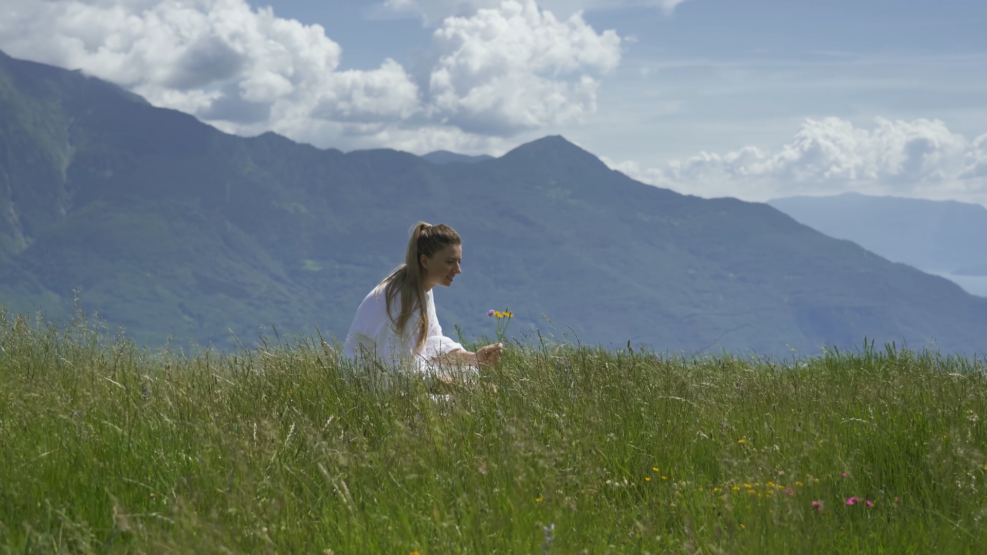 Woman picks flowers in front of mountains landscape