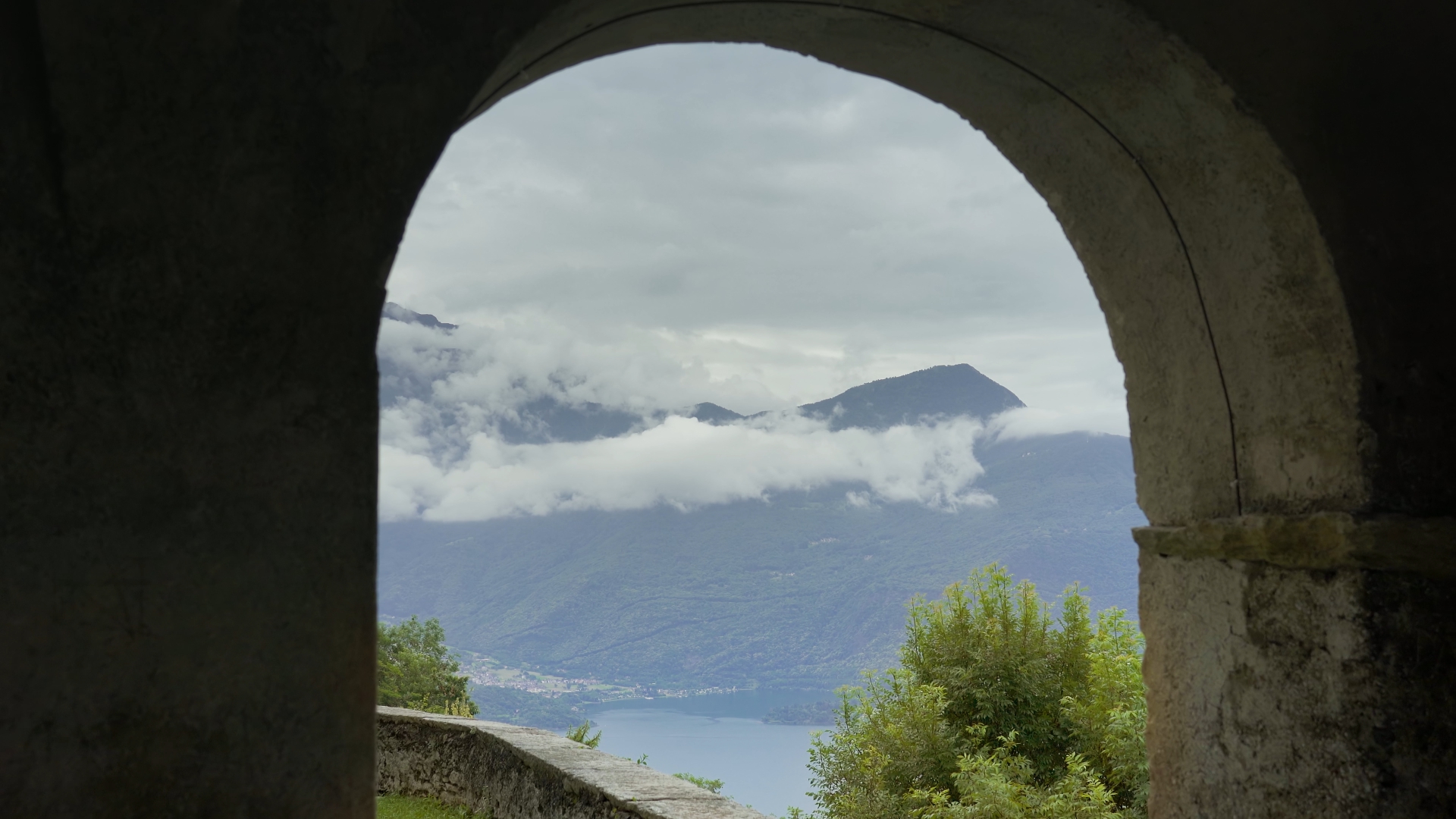 Cloud-capped mountains open up behind an ancient building arch
