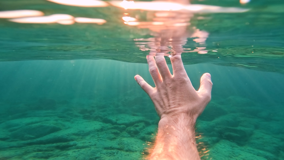 Mano sott’acqua illuminata da raggi solari