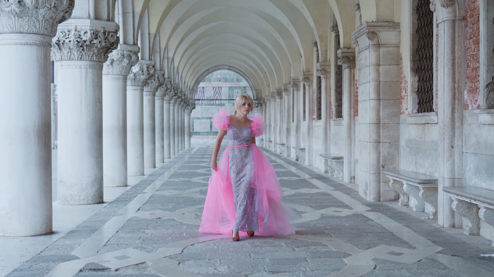 Donna in abito rosa cammina sotto portici di Venezia