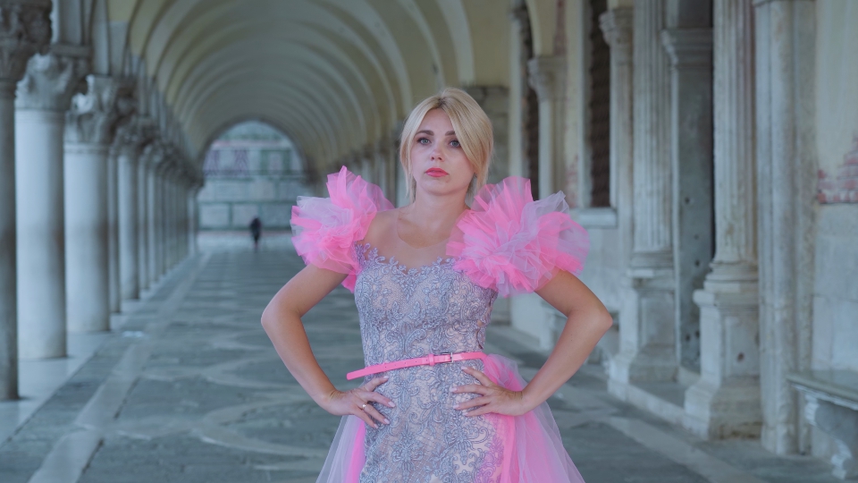 Woman in pink dress poses under ancient columns