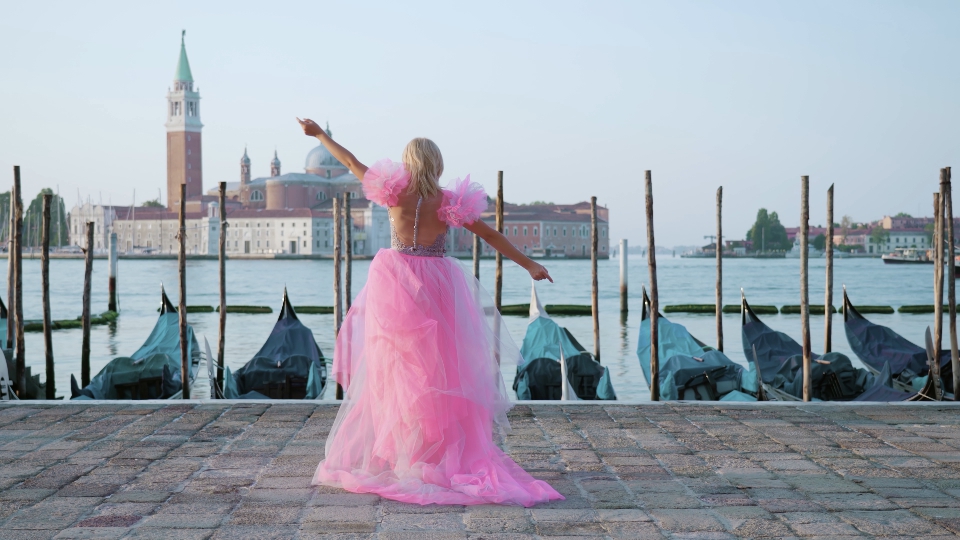 Donna con tacchi e vestito rosa cammina davanti gondole ormeggiate a Venezia