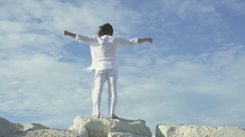 Uomo vestito di bianco sui sassi al vento