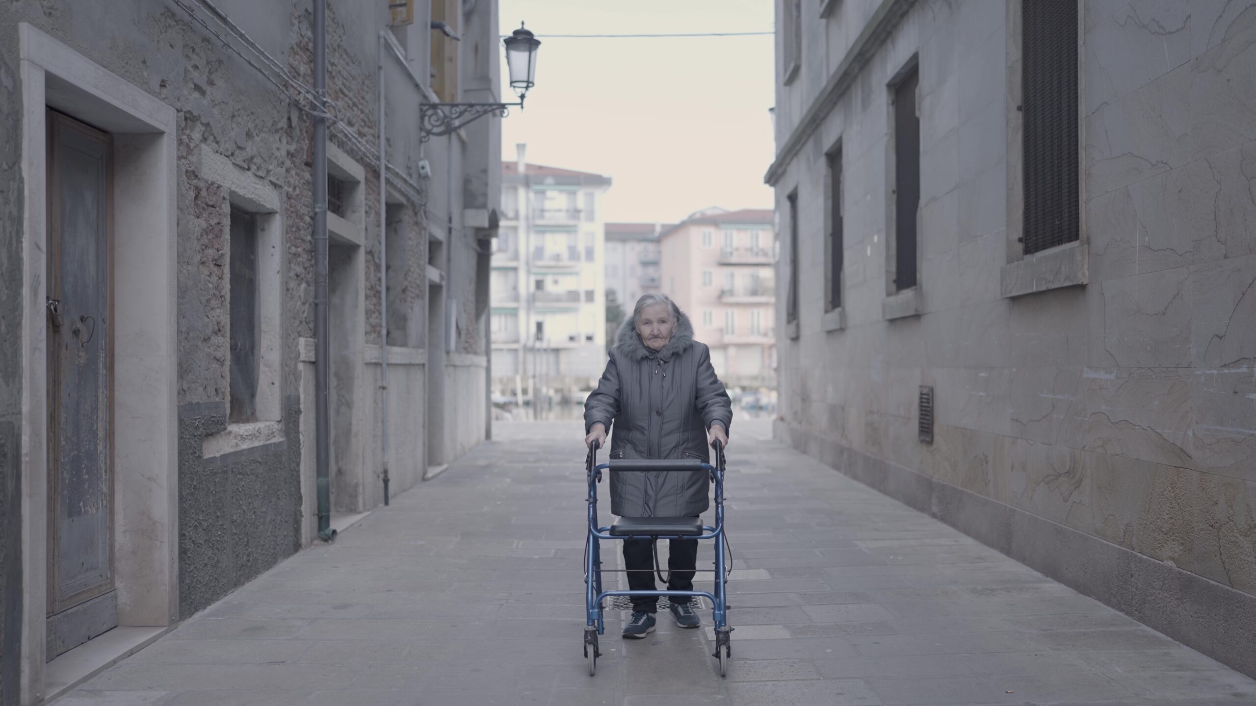 Elderly woman with walker navigating urban streets using her wheels on asphalt