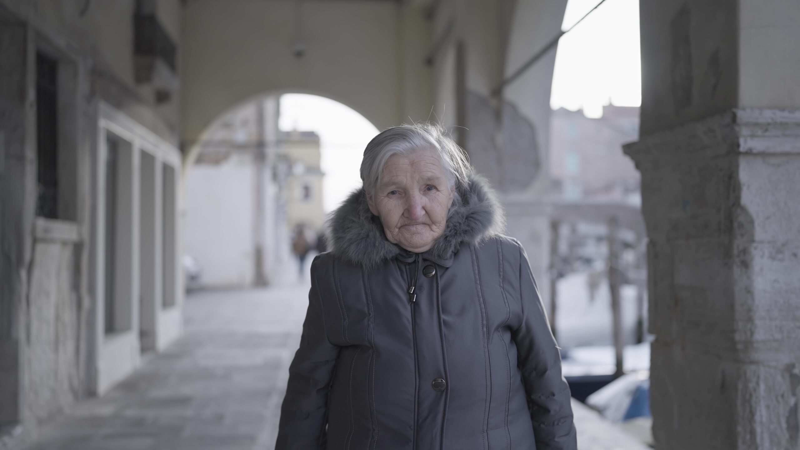 Elderly woman in coat under ancient building