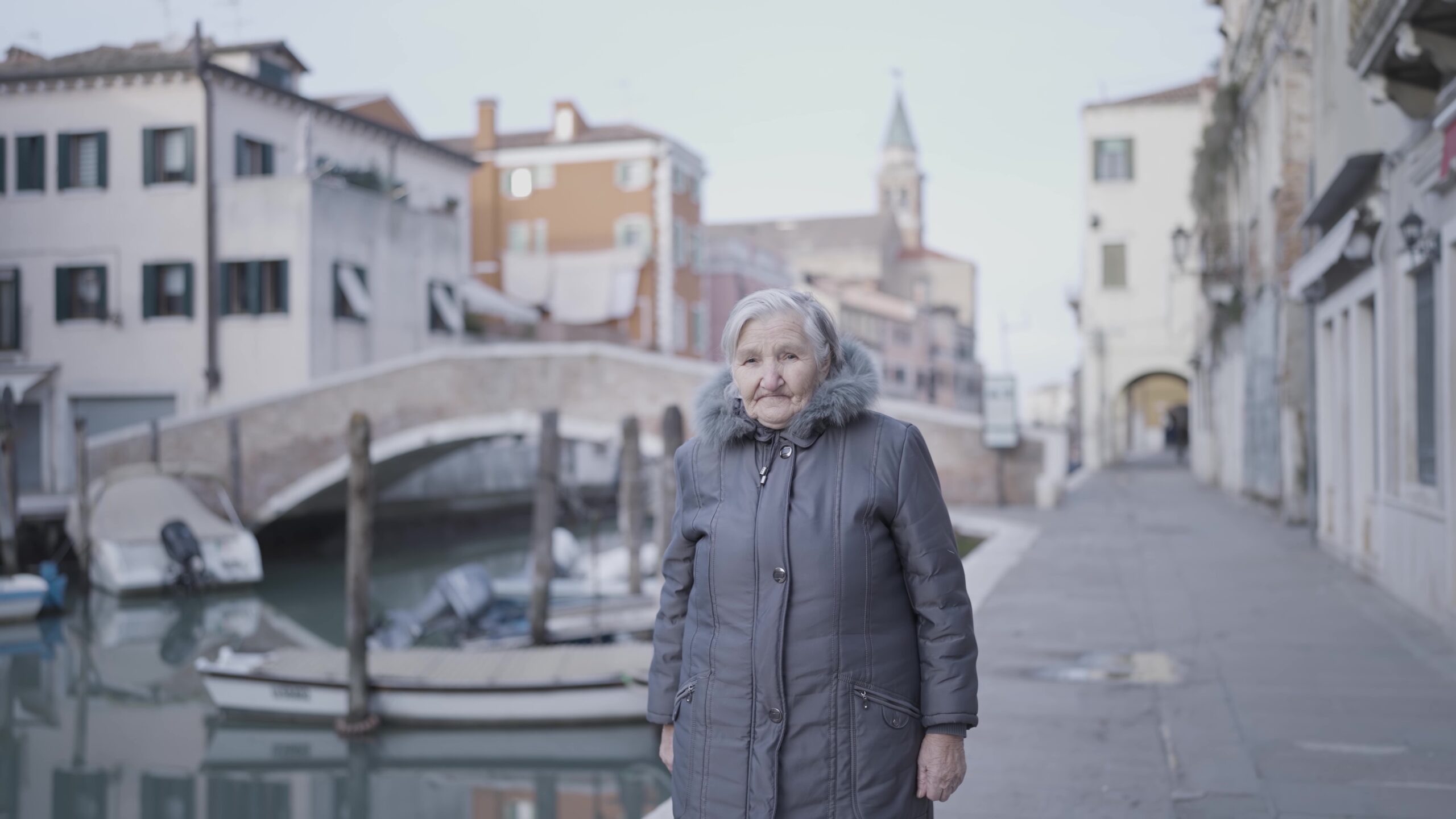 An elderly woman along a city street next to a body of water