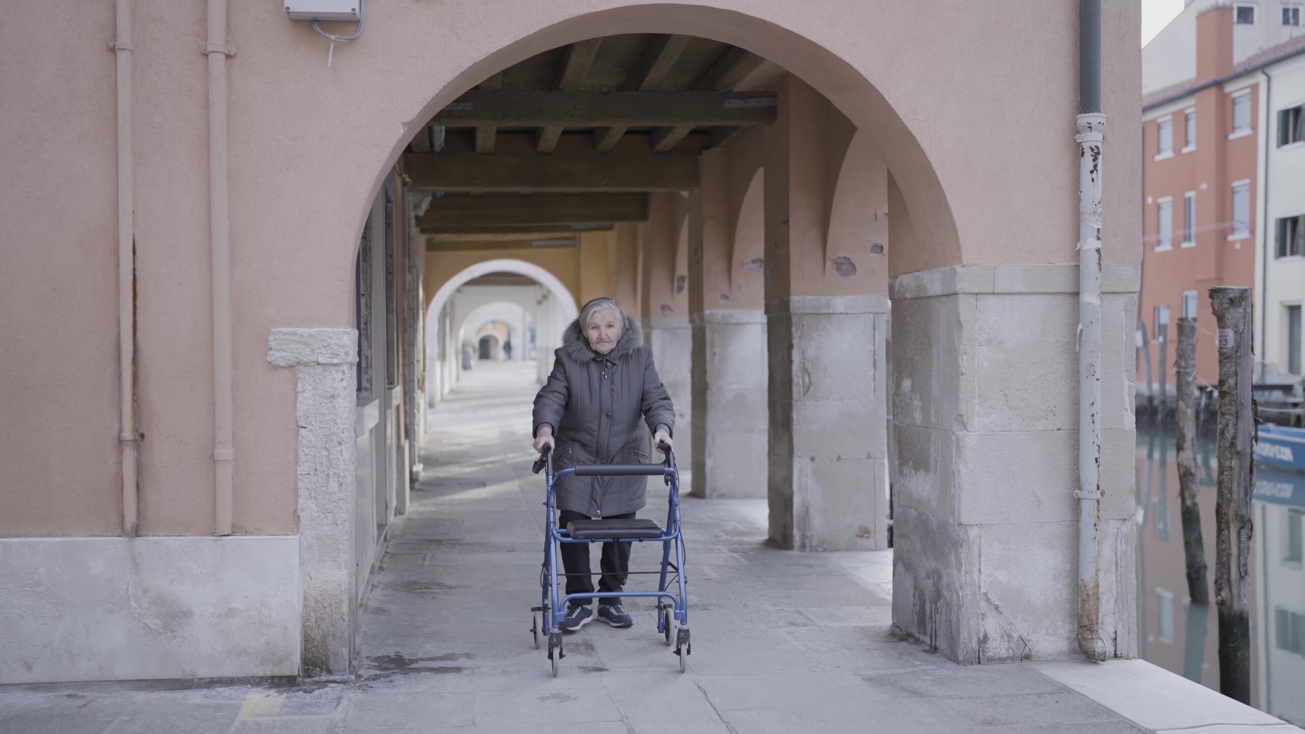 An elderly man using a walker near a building with artistic facade.