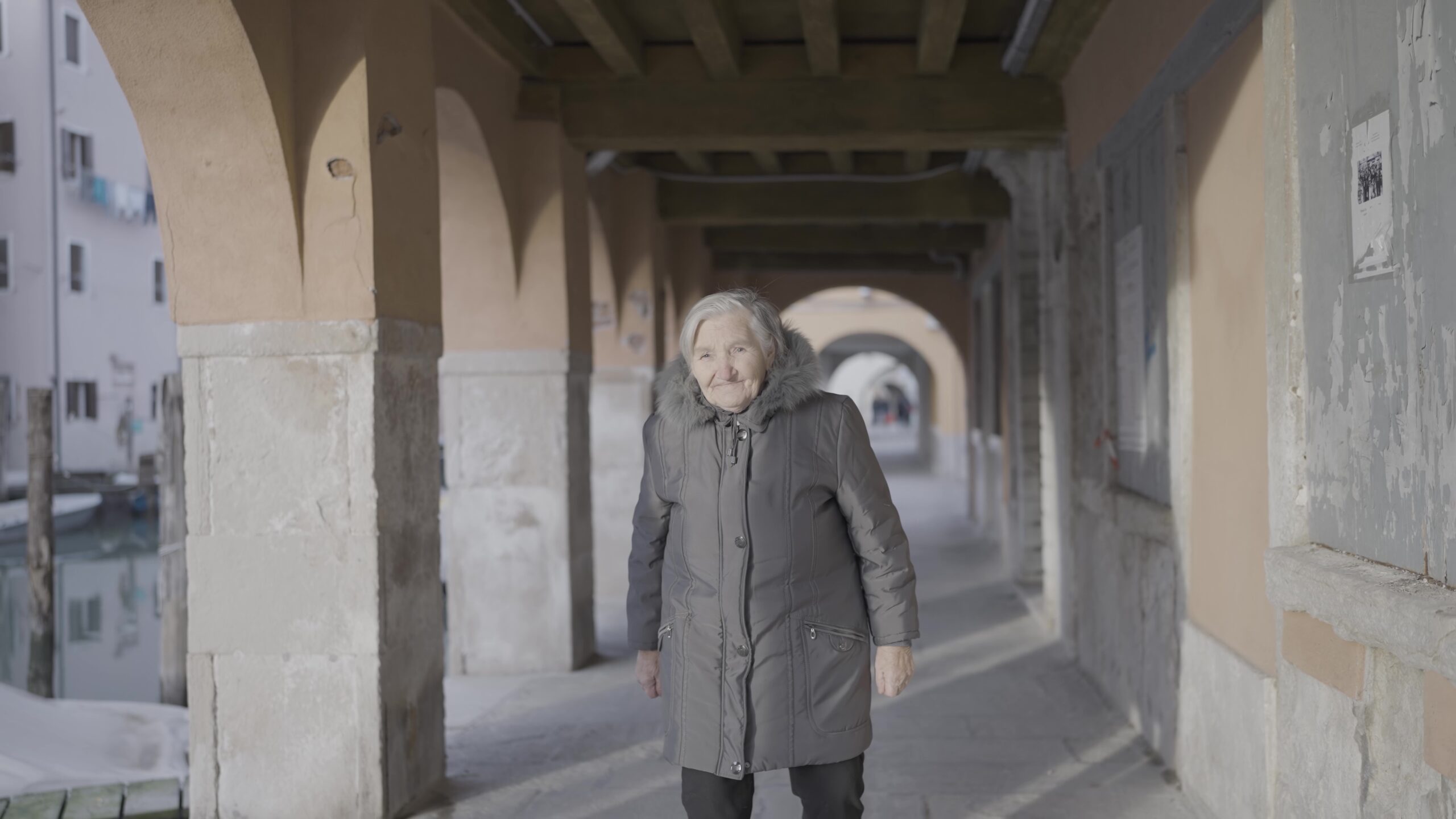 Una donna anziana sta camminando lungo un corridoio tra due edifici
