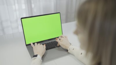 Donna che scrive sul computer portatile con schermo verde sul tavolo dell'ufficio