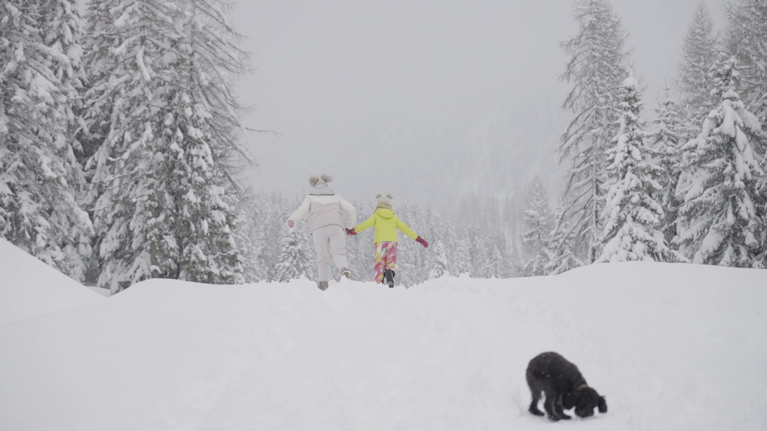 Mamma e figlia corrono sulla neve tenendosi per mano