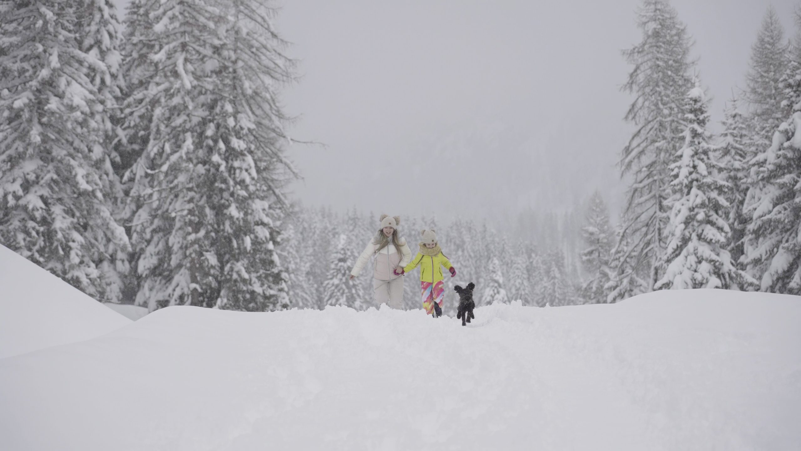 Mamma e figlia corrono con il cane sulla neve