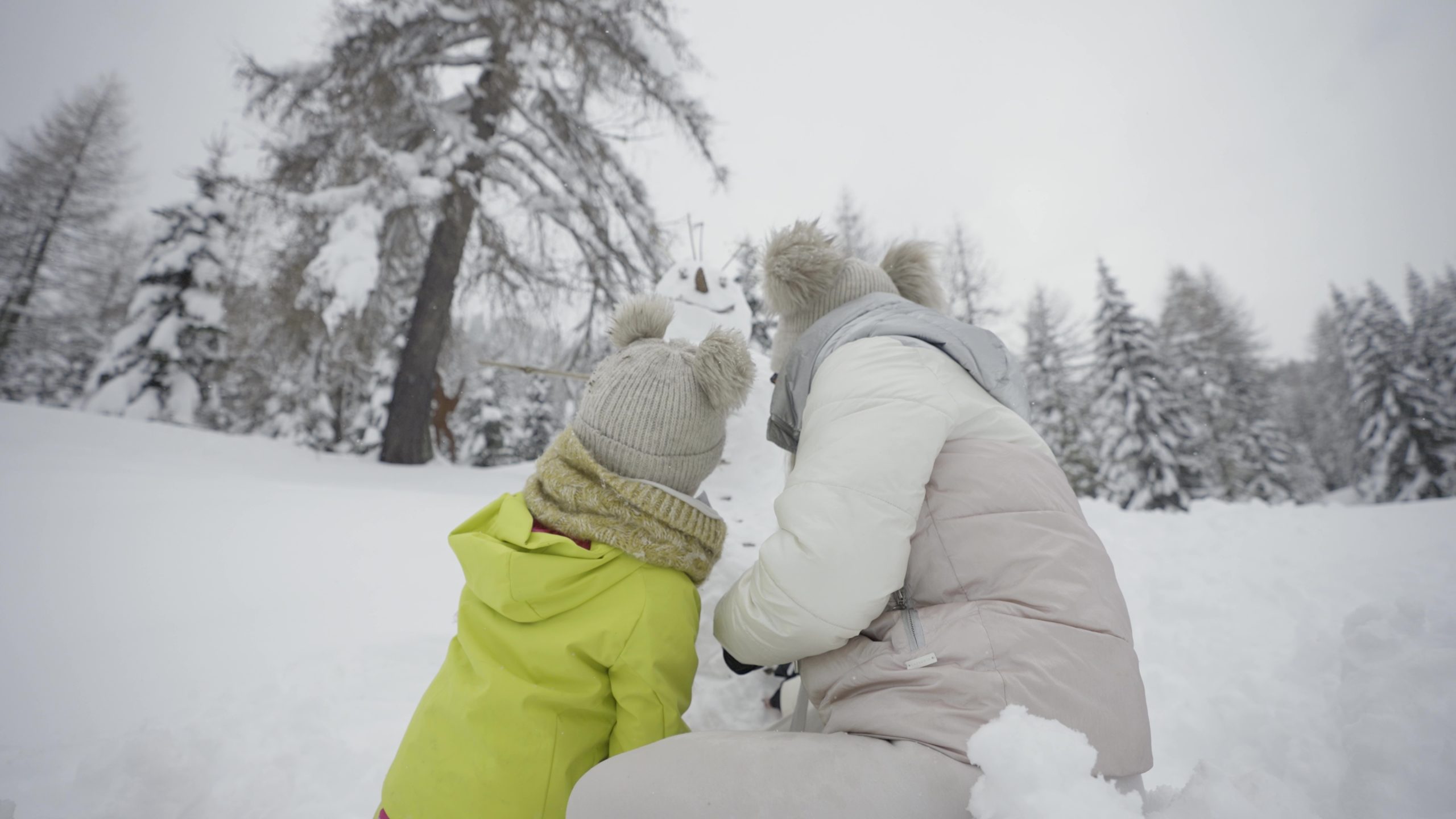 Mom and daughter are making snowman in winter