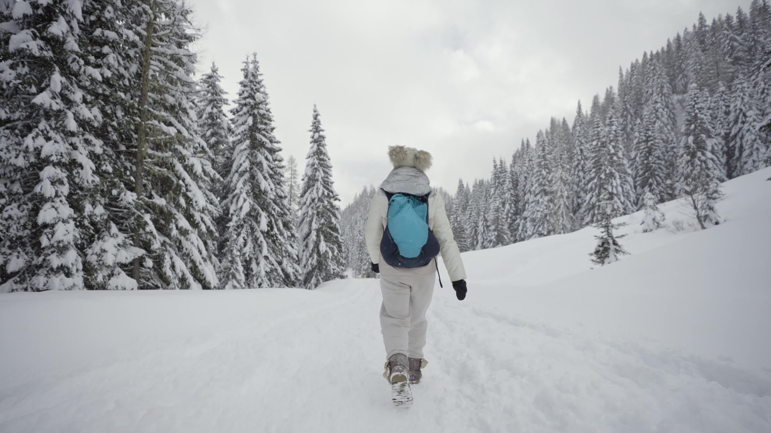 Woman walks on snow among fir trees