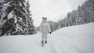 Woman dressed in white walks on path full of snow in the forest