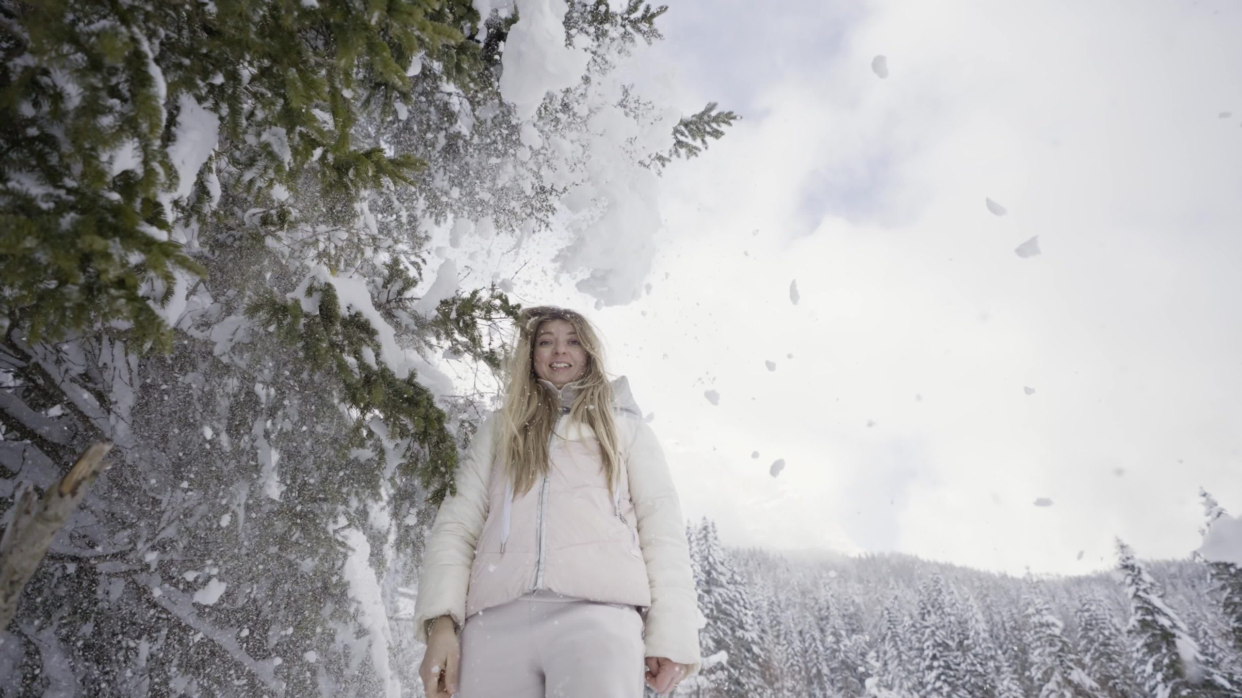 Snow from the tree falls on the head of the happy woman