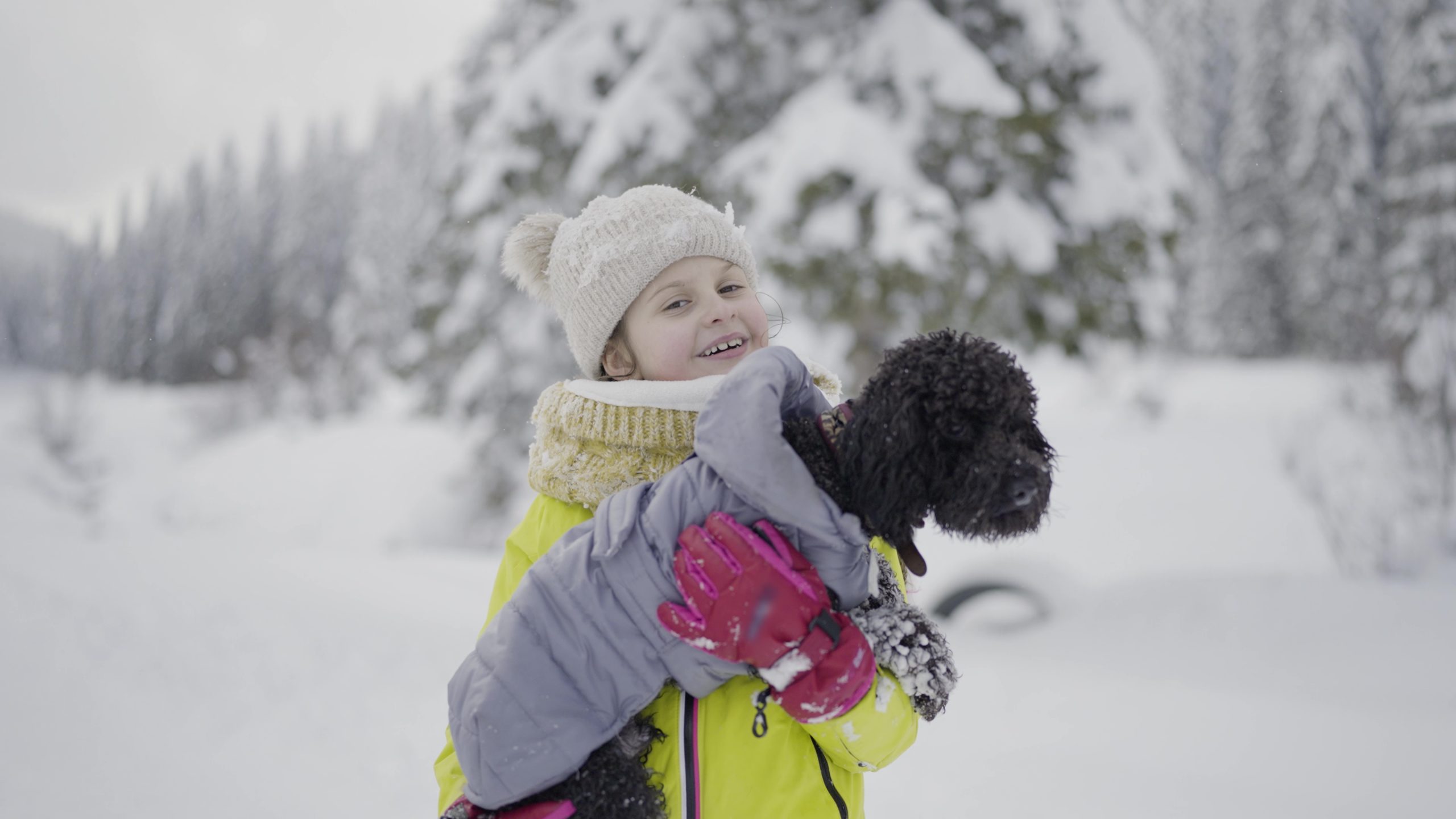 Little girl holds poodle dog in her arms in the snow