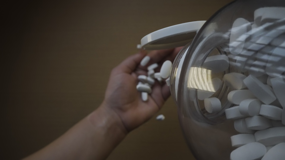 Mano che versa capsule bianche da un barattolo trasparente