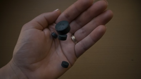 Hand Holding Black Charcoal Pills