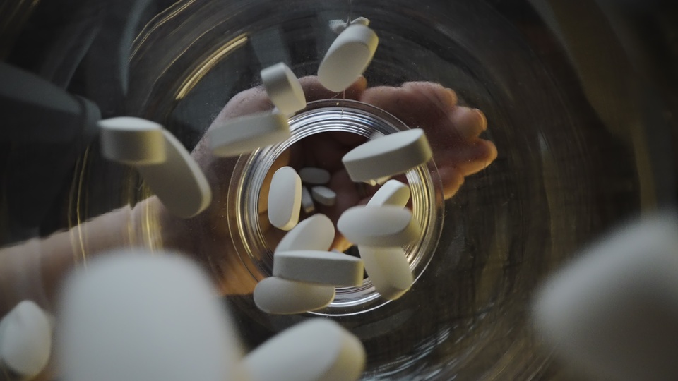White Pills Dropping into a Transparent Jar
