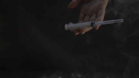 Mano che tiene una siringa nel fumo scuro