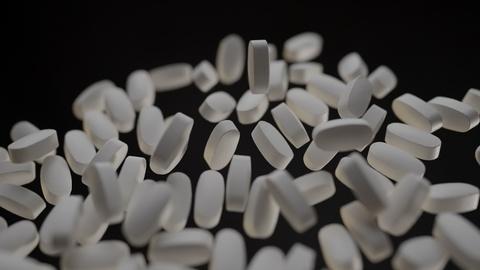 White Pills Falling Against Black Background