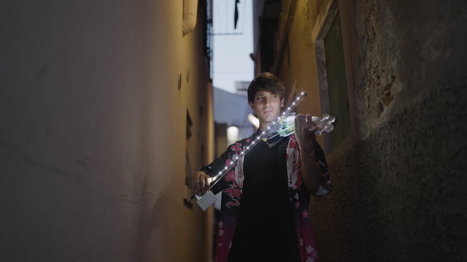Man playing illuminated violin in narrow alley