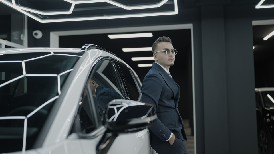Man in suit leaning against a luxury car in modern showroom