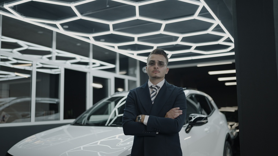 Uomo d’affari sicuro di sé accanto a un’auto di lusso in uno showroom futuristico
