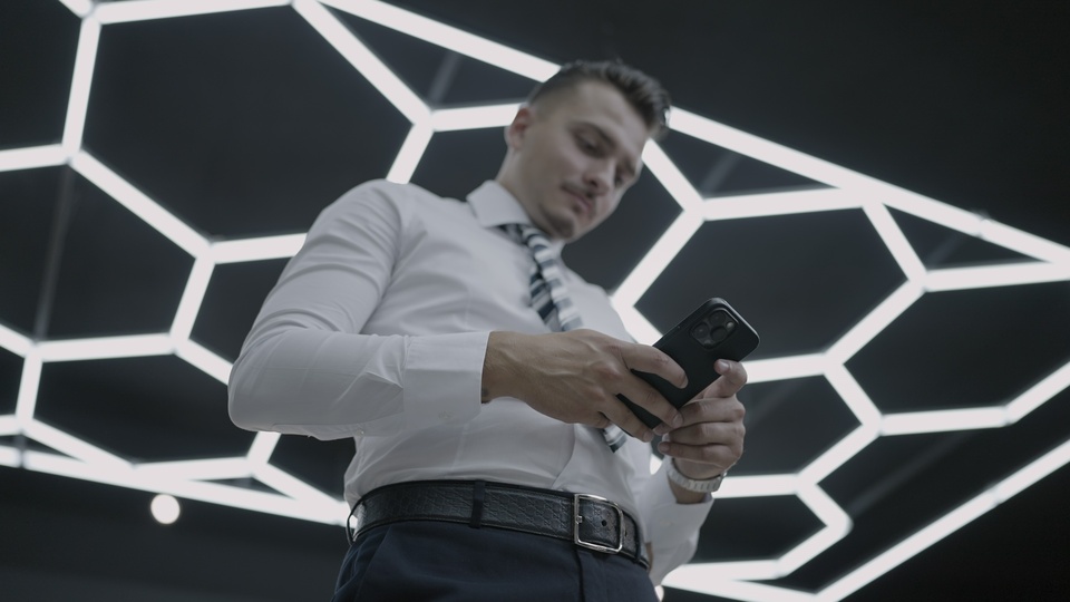Uomo d’affari che controlla il telefono sotto un’illuminazione moderna