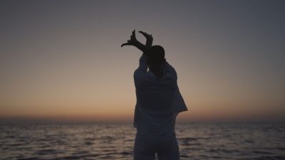 Silhouette of a person stretching arms at sunset by the sea