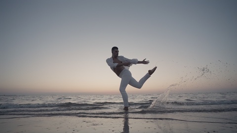 Person performing dynamic movement by the sea at sunset