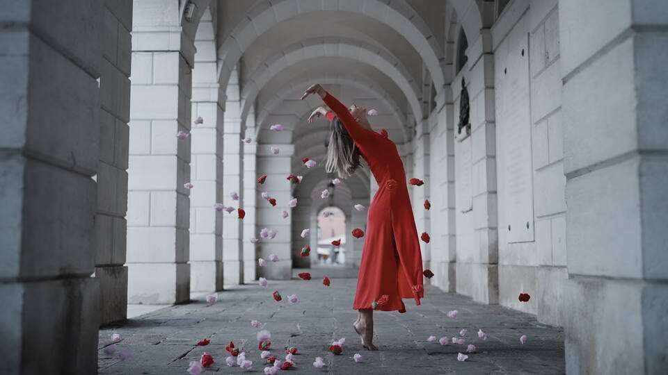 Ballerina in abito rosso circondata da petali cadenti