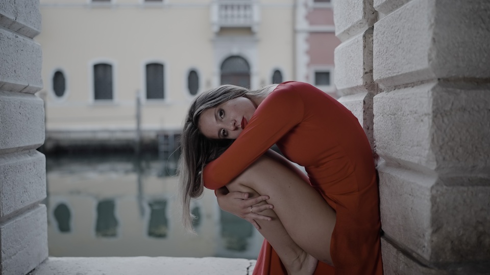 Donna riflessiva in abito rosso vicino all’acqua