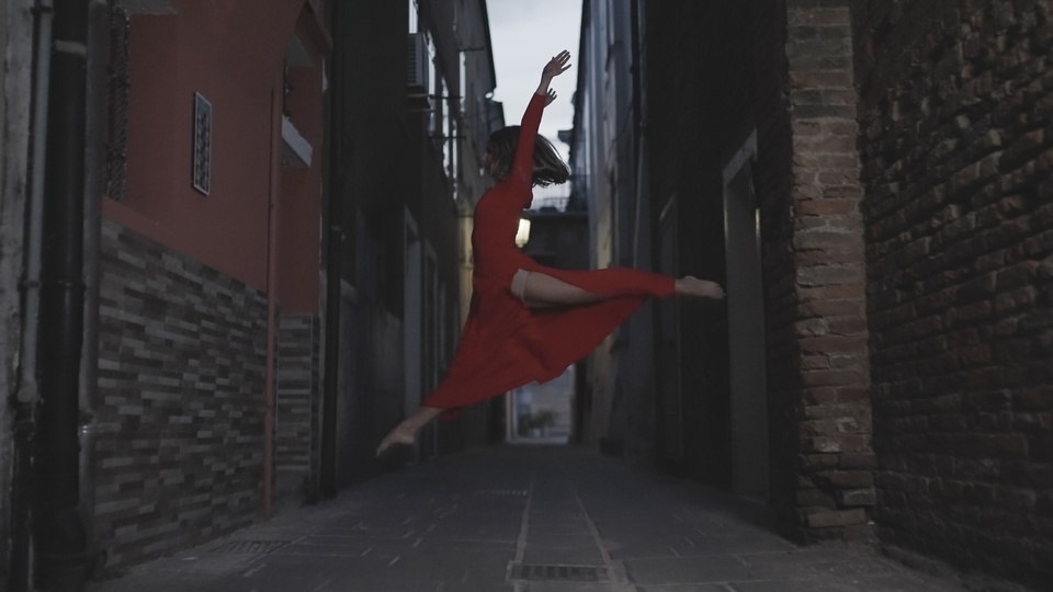 Dancer in Red Performing a Leap in Urban Alley