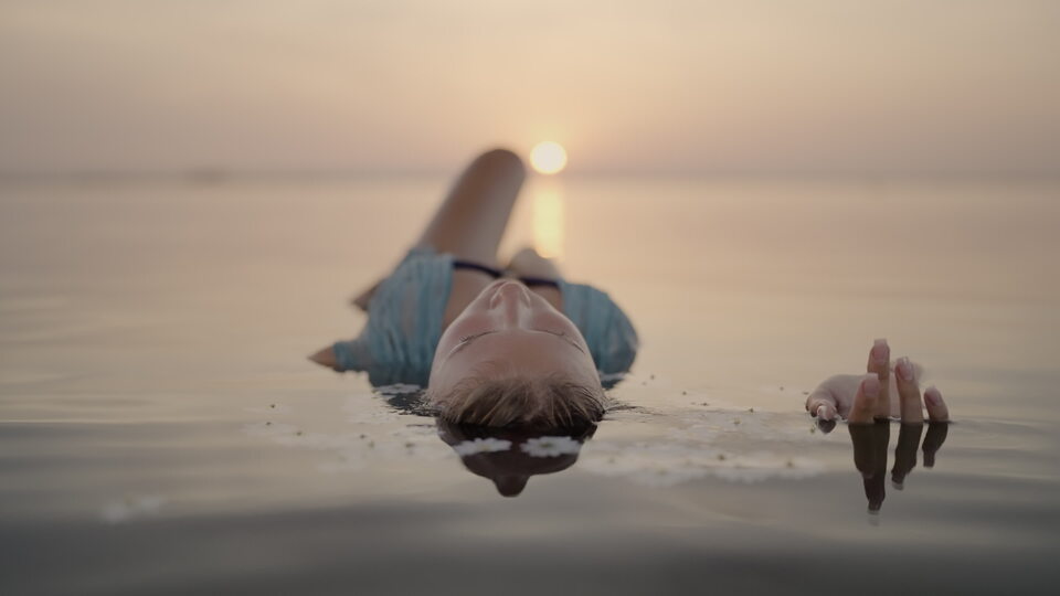 Donna che galleggia nell’acqua calma al tramonto