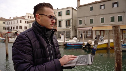 Man Walking While Working on Laptop by Canal
